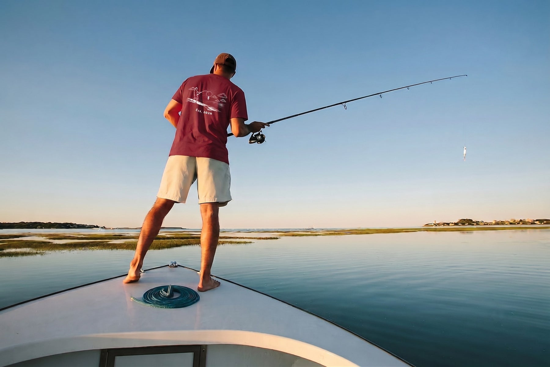 Angler casting from the bow of a boat in the burgundy Fishing Man tee