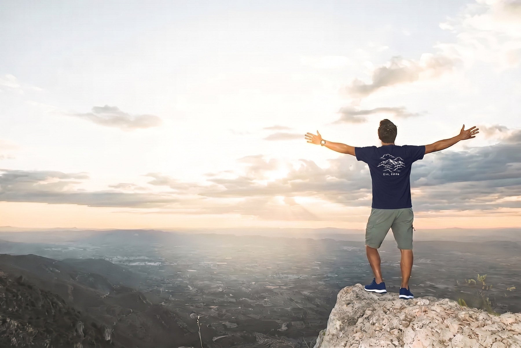 Man in the True Navy Mountains in the Clouds tee standing on a summit at sunrise with arms outstretched